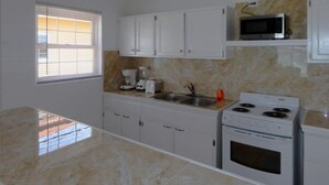 Una cocina con armarios blancos, estufa, microondas y una ventana con persianas.