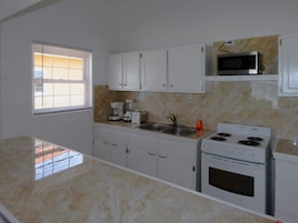 A kitchen with white cabinets, a stove, a microwave, and a window with blinds.