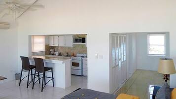 Una cocina moderna con armarios blancos, microondas y estufa. Hay un comedor con dos sillas y una mesa.
