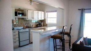 Una cocina con gabinetes blancos, microondas, estufa y un taburete de bar.