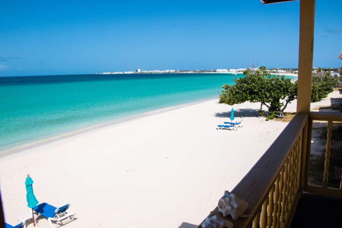 Une plage avec du sable blanc, une eau turquoise et limpide, et quelques arbres.