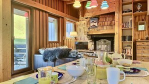 Interior acolhedor de uma cabana com uma mesa de jantar posta para o café da manhã, lareira e paredes de madeira.
