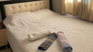 En pænt redt seng med hvid dyne, to sammenrullede håndklæder og en Samsung luftkonditionering ovenover.