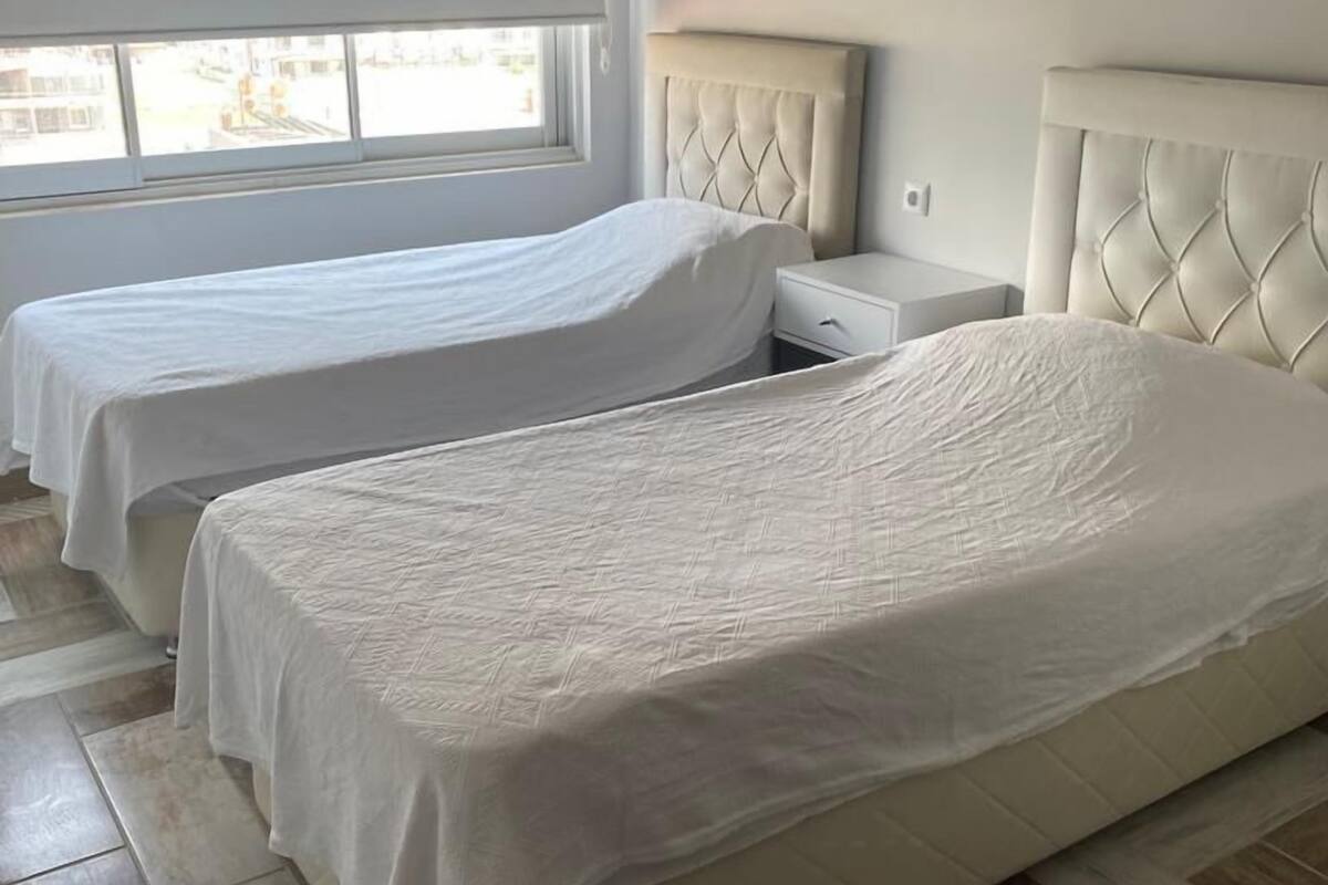 Une chambre d’hôtel avec deux lits, une fenêtre et un sol carrelé.