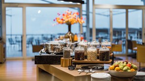 A buffet setup with various food containers, a fruit bowl, and a sign indicating fruit selection. - Hôtel Palafitte (Neuchatel)