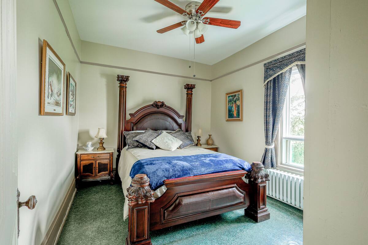 A bedroom with a wooden bed, a ceiling fan, a window with curtains, and a radiator.