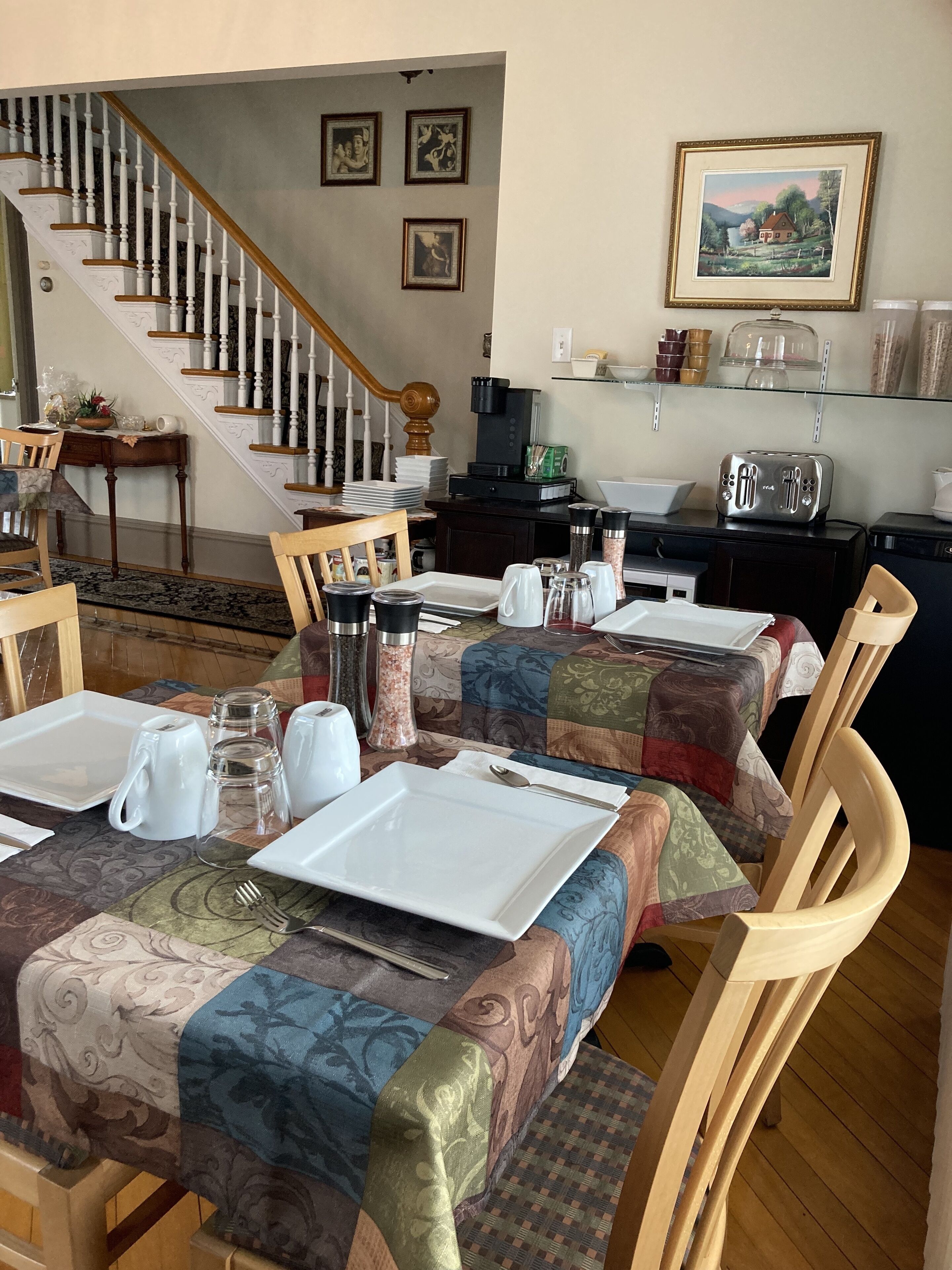 Comedor con una mesa lista para cuatro, una escalera y un área de cocina con tostadora y cafetera.