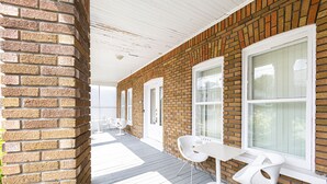 Eine überdachte Veranda mit Backsteinwand, weißen Fenstern und einem Tisch mit zwei Stühlen.