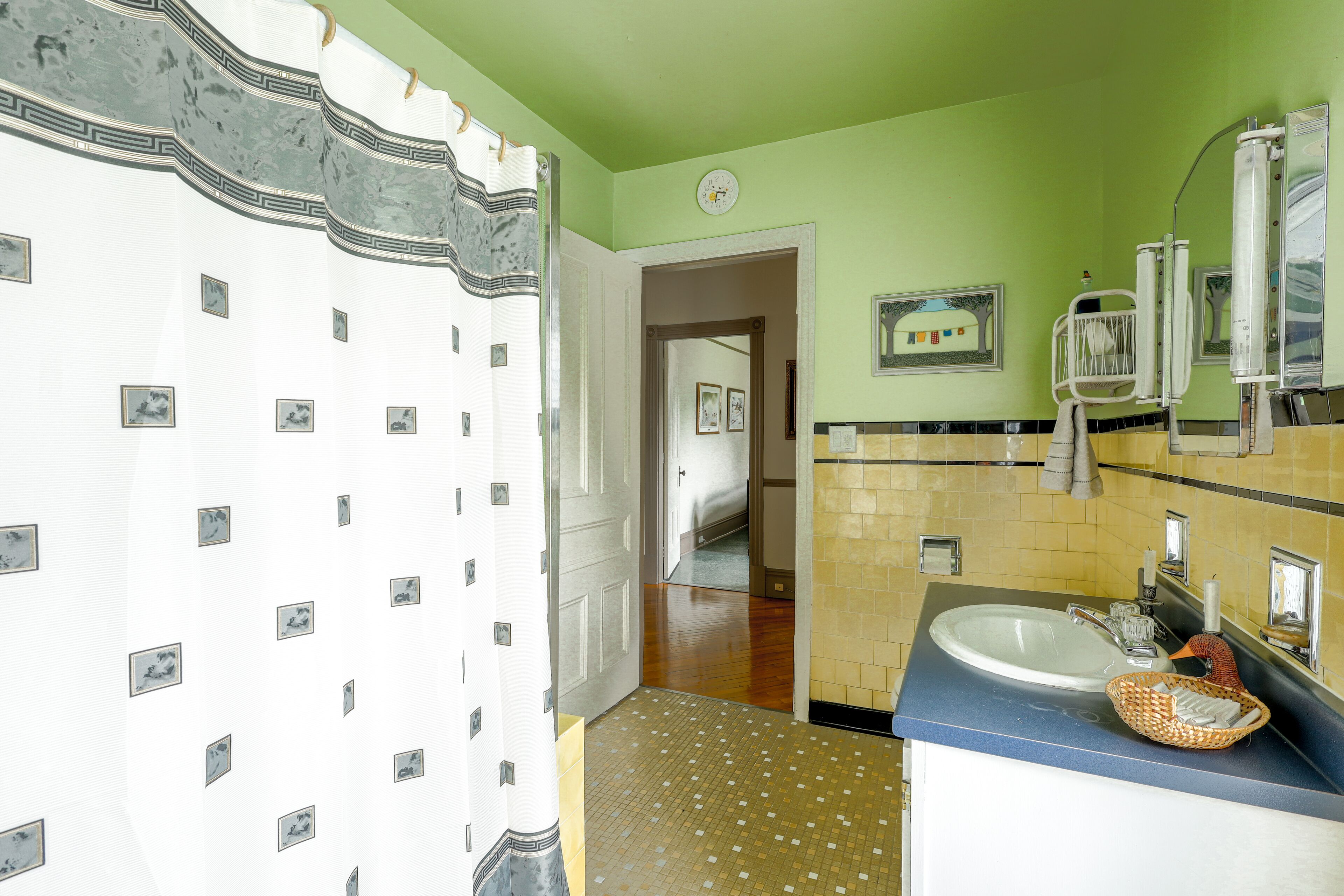 A bathroom with a white shower curtain, a sink with a mirror, and a tiled floor.