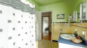 A bathroom with a white shower curtain, a sink with a mirror, and a tiled floor.