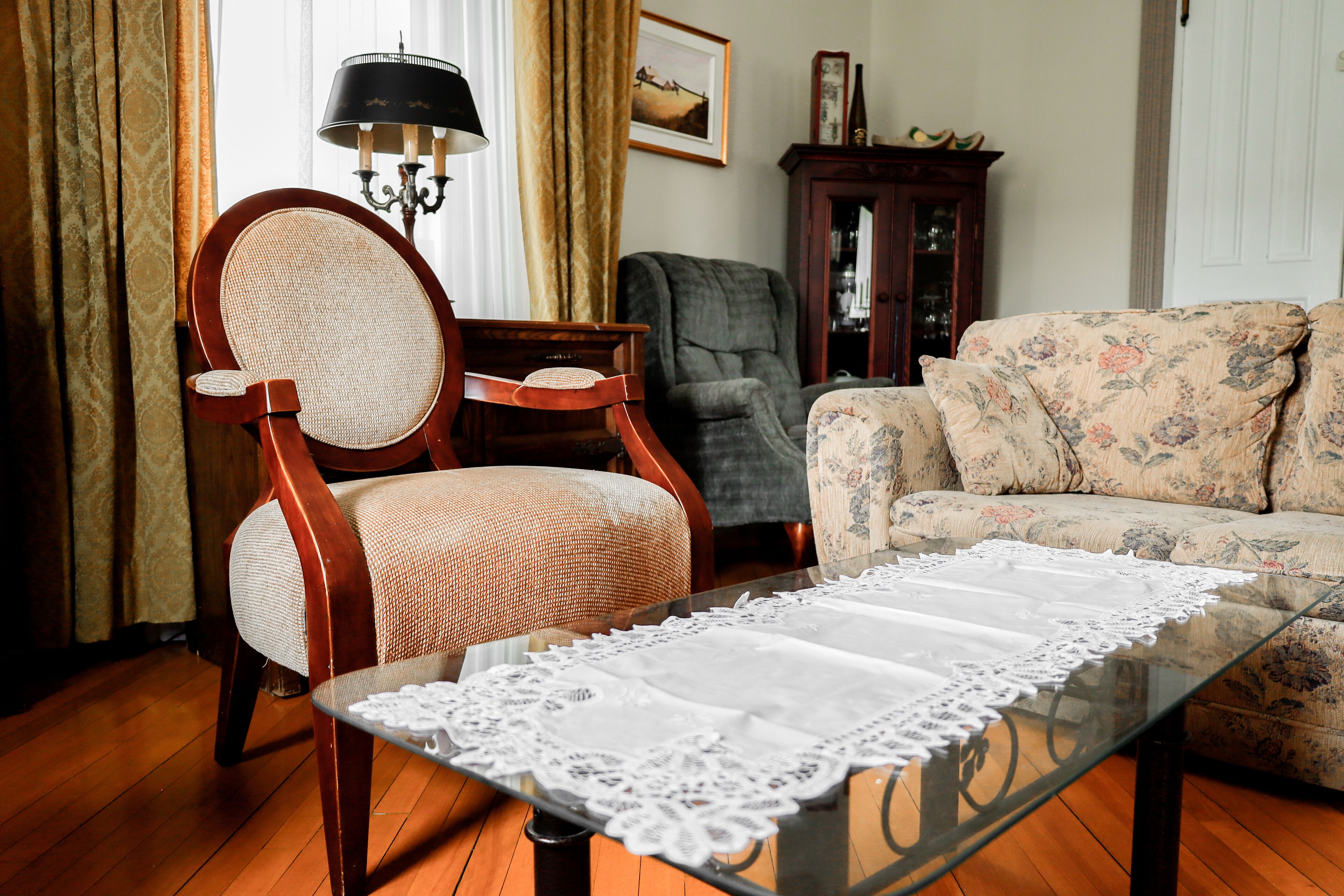 A living room with a glass coffee table, a wooden chair, a sofa, a lamp, and a cabinet.