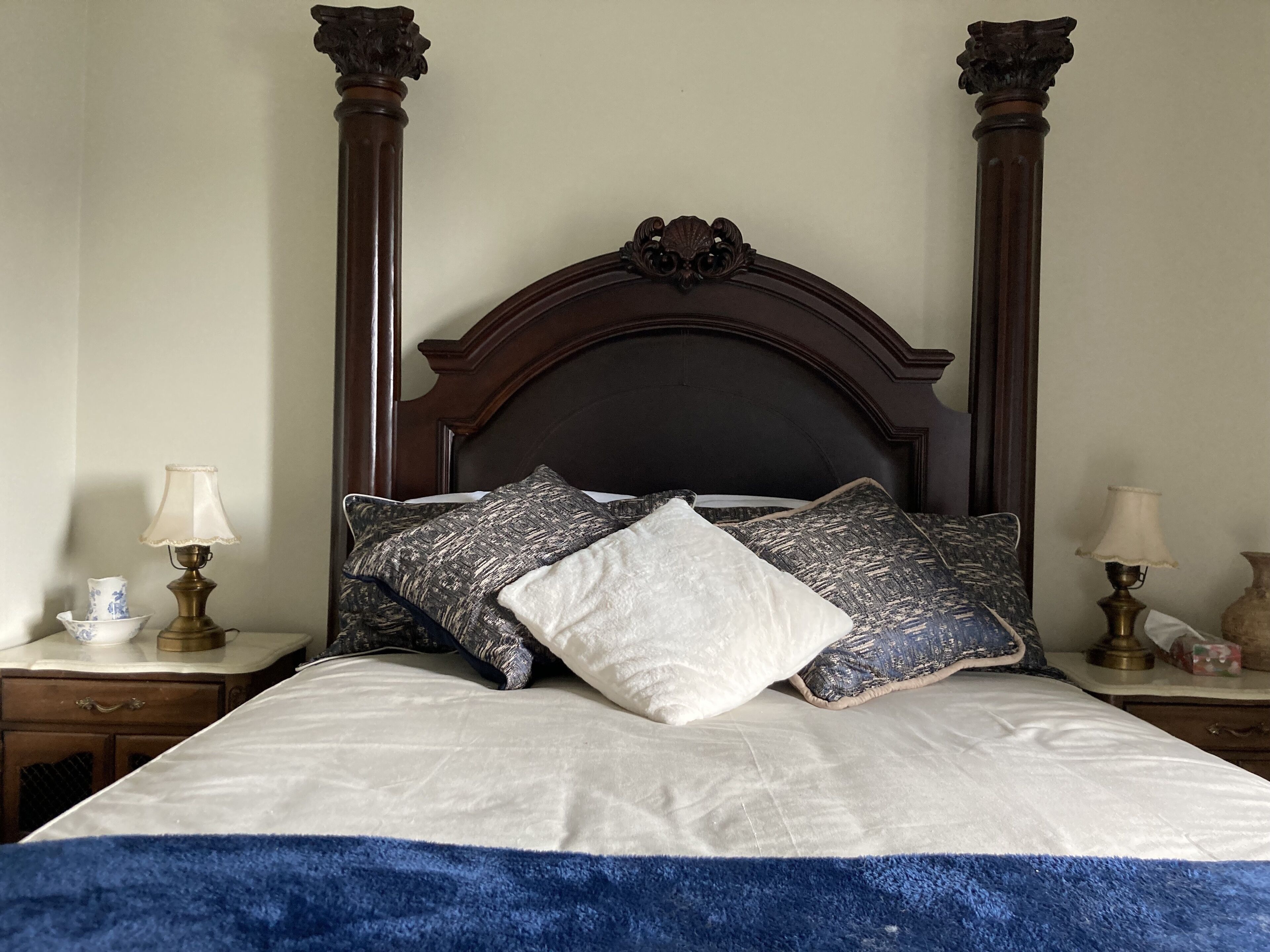 Een bed met een donker hoofdeinde, twee nachtkastjes met lampen en een blauwe plaid.