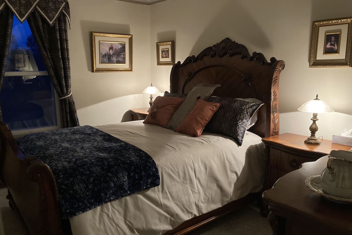 A neatly made bed with a wooden headboard, two bedside tables with lamps, and framed pictures on the walls.