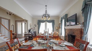 Ein Esszimmer mit einem großen Tisch, gedeckt für sechs Personen, umgeben von Holzstühlen, einem Kamin und einem an der Wand befestigten Fernseher.