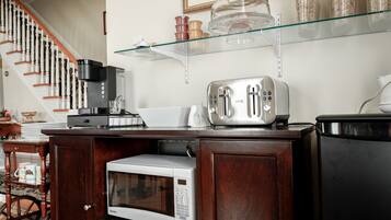 A kitchen with a microwave, toaster, coffee maker, and a glass shelf above a cabinet.