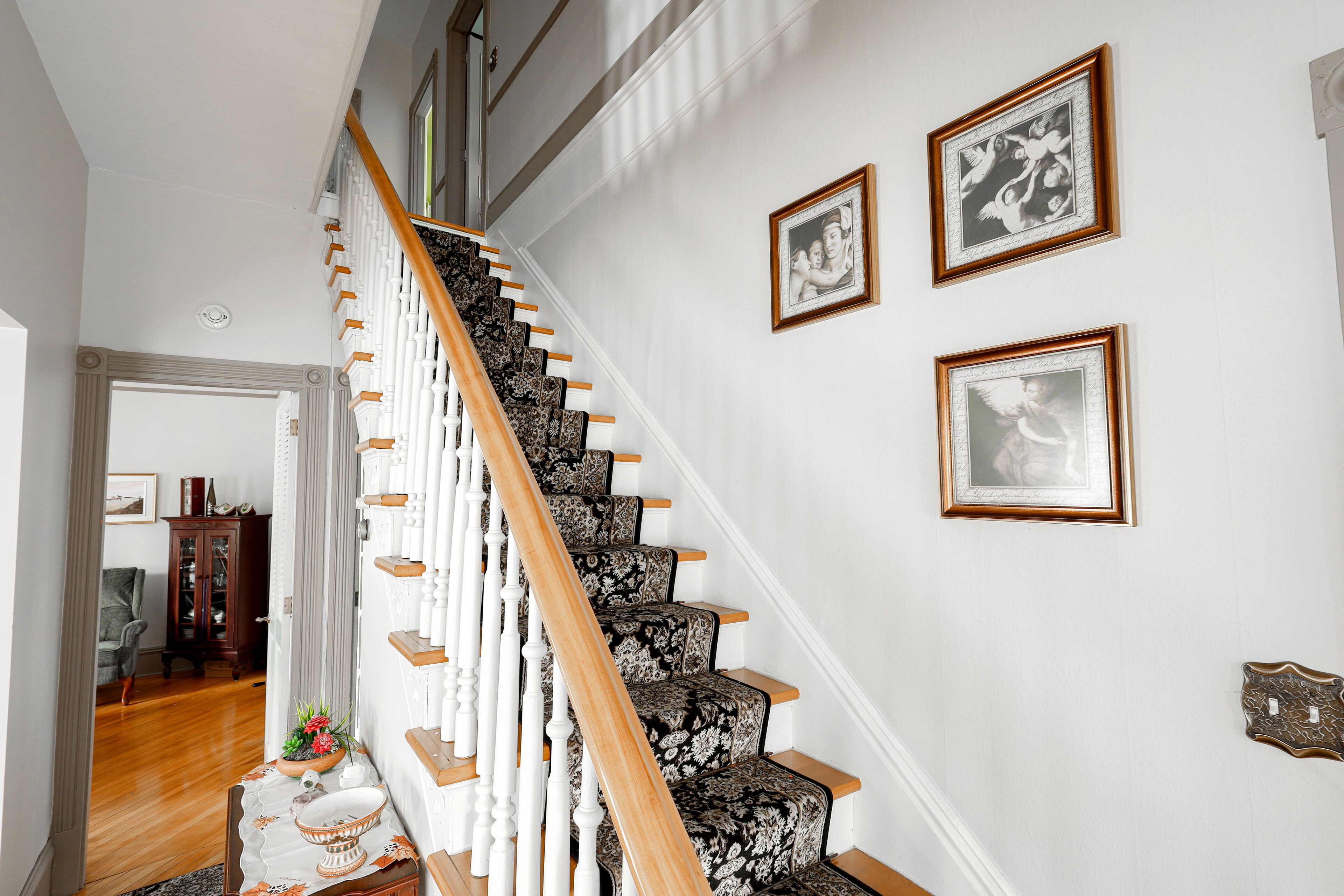 Una escalera con peldaños cubiertos de un estampado de alfombra y barandales de madera, que conduce a un piso superior.