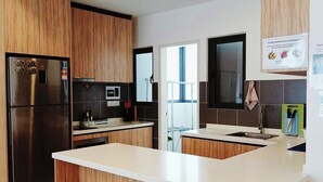 A modern kitchen with wooden cabinets, a stainless steel refrigerator, a built-in oven, and a large island with a bench. - The OakHome Lakecity @ KL Taman Wahyu 3-bedroom Poolview! (Batu Caves)