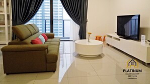 A modern living room with a sofa, a coffee table, a TV, and a view of a cityscape through large windows. - The OakHome Lakecity @ KL Taman Wahyu 3-bedroom Poolview! (Batu Caves)
