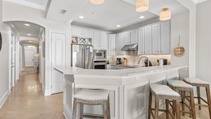A modern kitchen with white cabinetry, a large island with stools, stainless steel appliances, and pendant lighting. - Villa Coyaba 306 | Private Beachfront | Includes Daily Beach Setup | Pool (Destin)