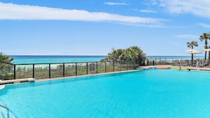 A clear blue pool with a view of the ocean, surrounded by palm trees and lounge chairs. - Villa Coyaba 306 | Private Beachfront | Includes Daily Beach Setup | Pool (Destin)