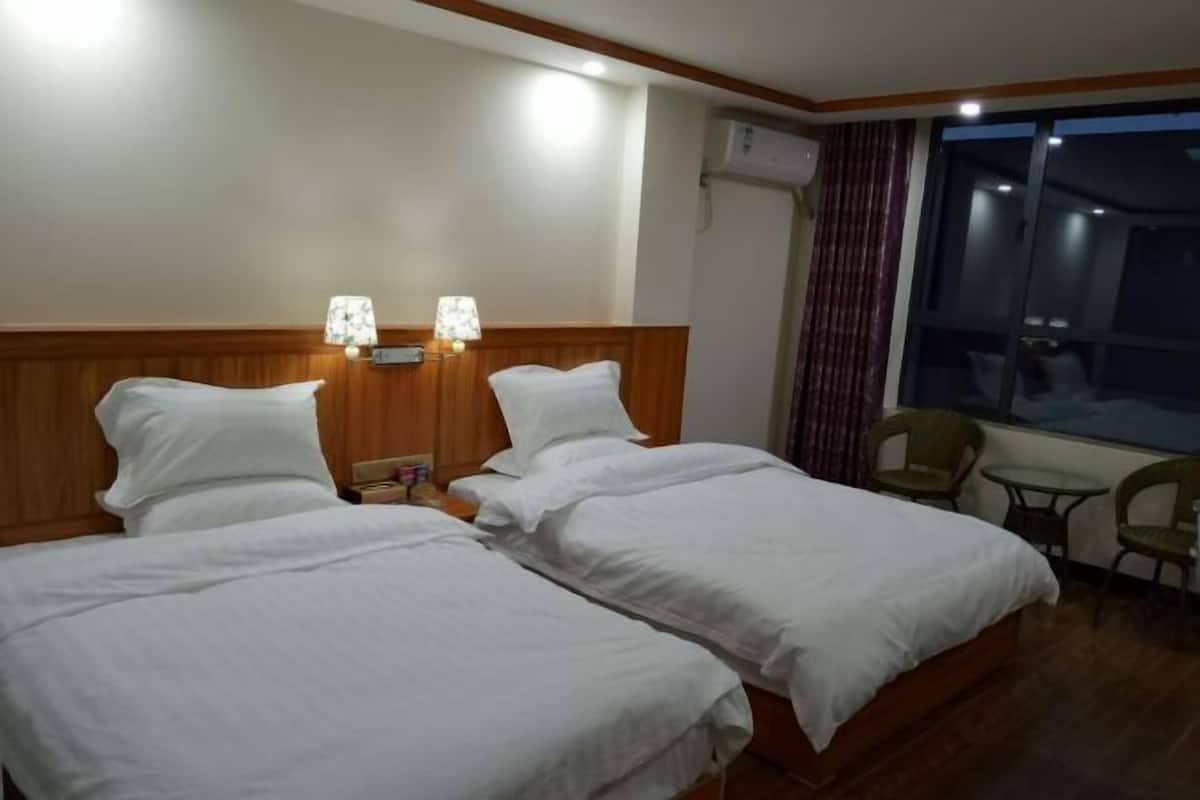 Habitación de hotel con dos camas, cabecero de madera, dos lámparas fijadas a la pared, una mesita y una ventana con cortinas.