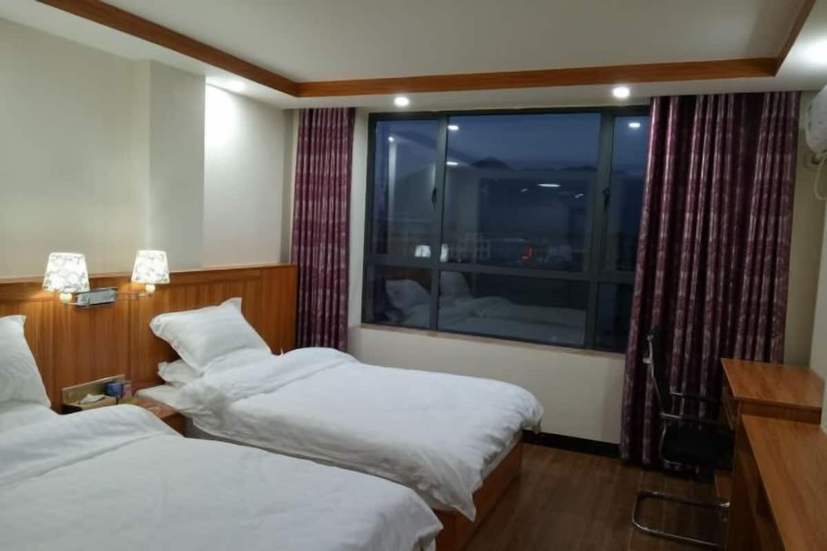 Habitación de hotel con dos camas, un escritorio, una silla, un ventanal con cortinas y lámparas fijadas a la pared.