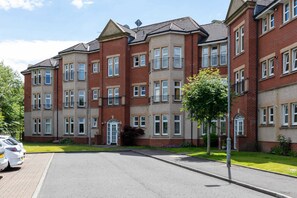A multi-story residential building with a brick facade, multiple windows, and a paved driveway.