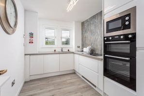 Una cocina moderna con armarios blancos, un horno doble, un microondas y una ventana con persianas.
