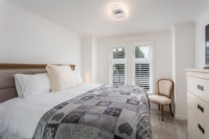 Un dormitorio con una cama, una silla, un aparador y una ventana con persianas.