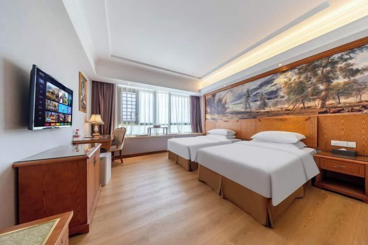 A hotel room with two beds, a desk, a TV, and a painting on the wall.