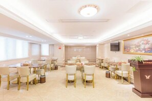 Une salle à manger d’hôtel avec des tables et des chaises, un téléviseur accroché au mur et un tableau.