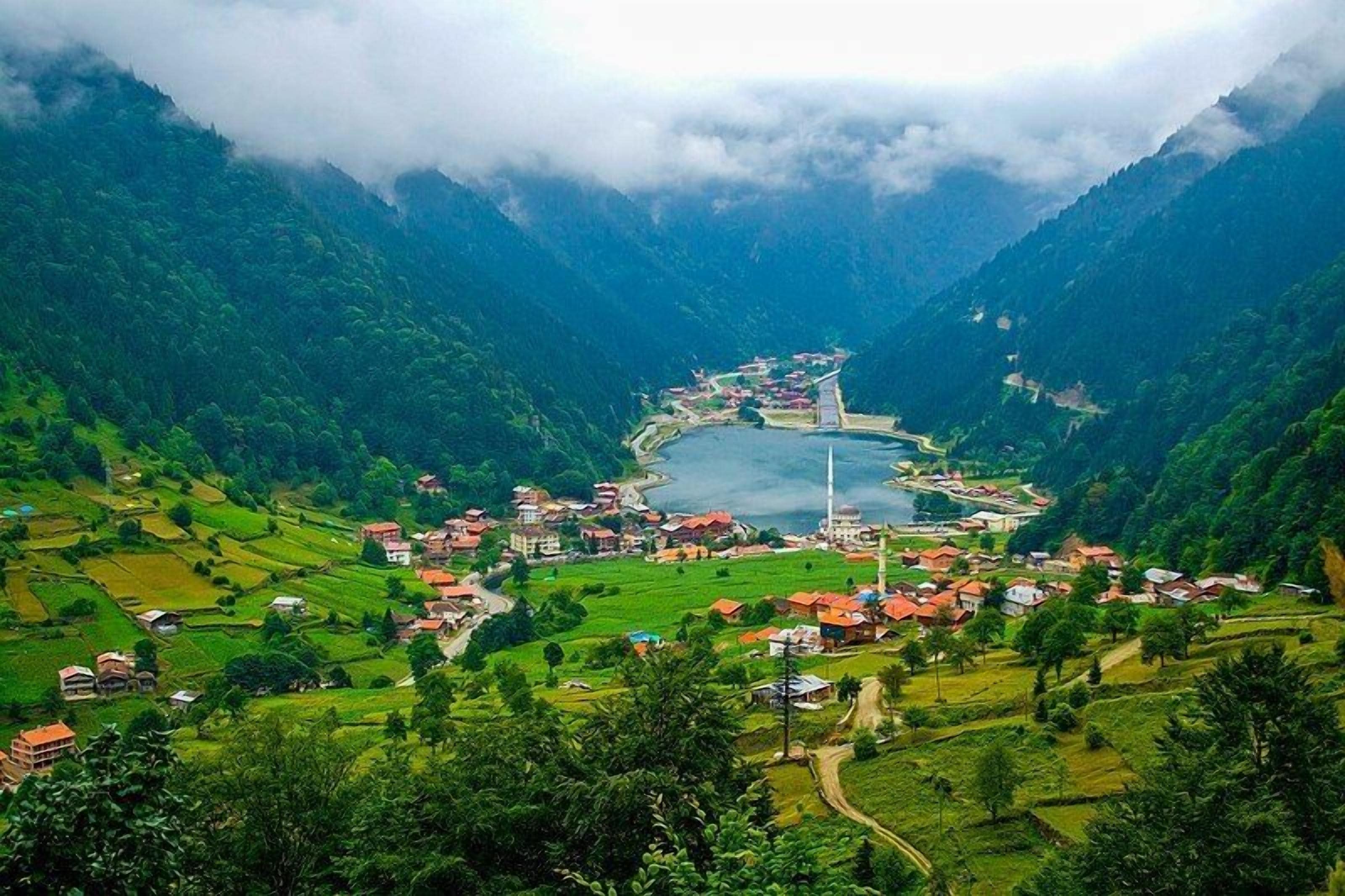 A mountainous village with terraced fields, a mosque, and a bridge over a river.