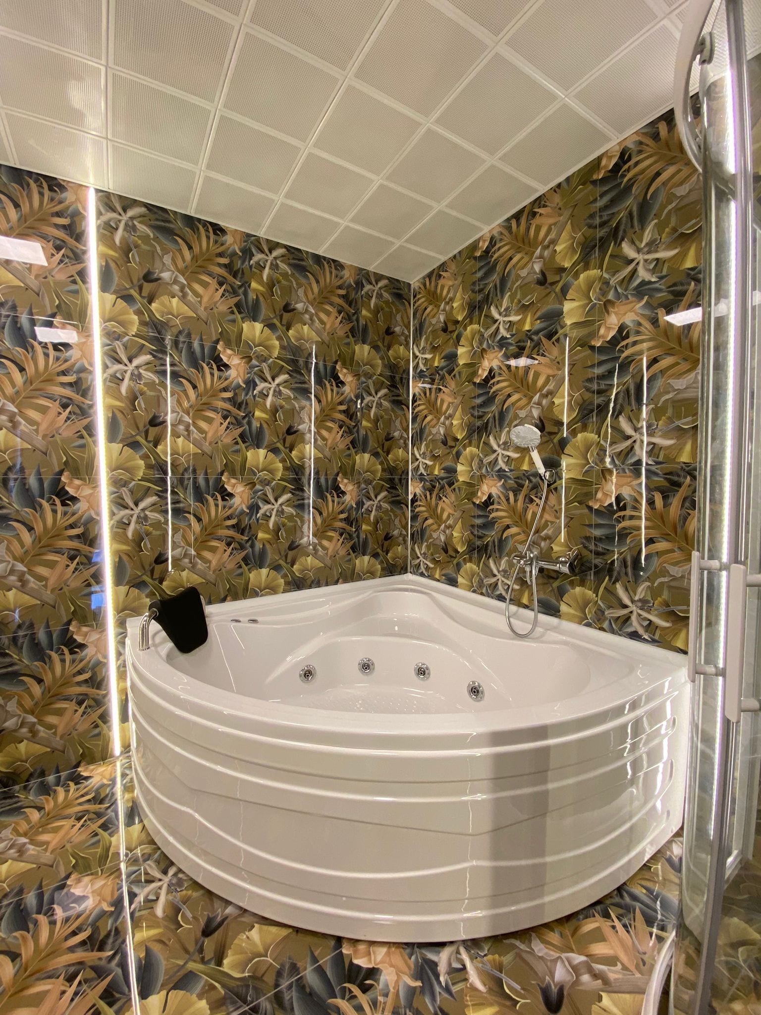 A modern bathroom with a freestanding bathtub, a shower area, and decorative leaf-patterned walls.