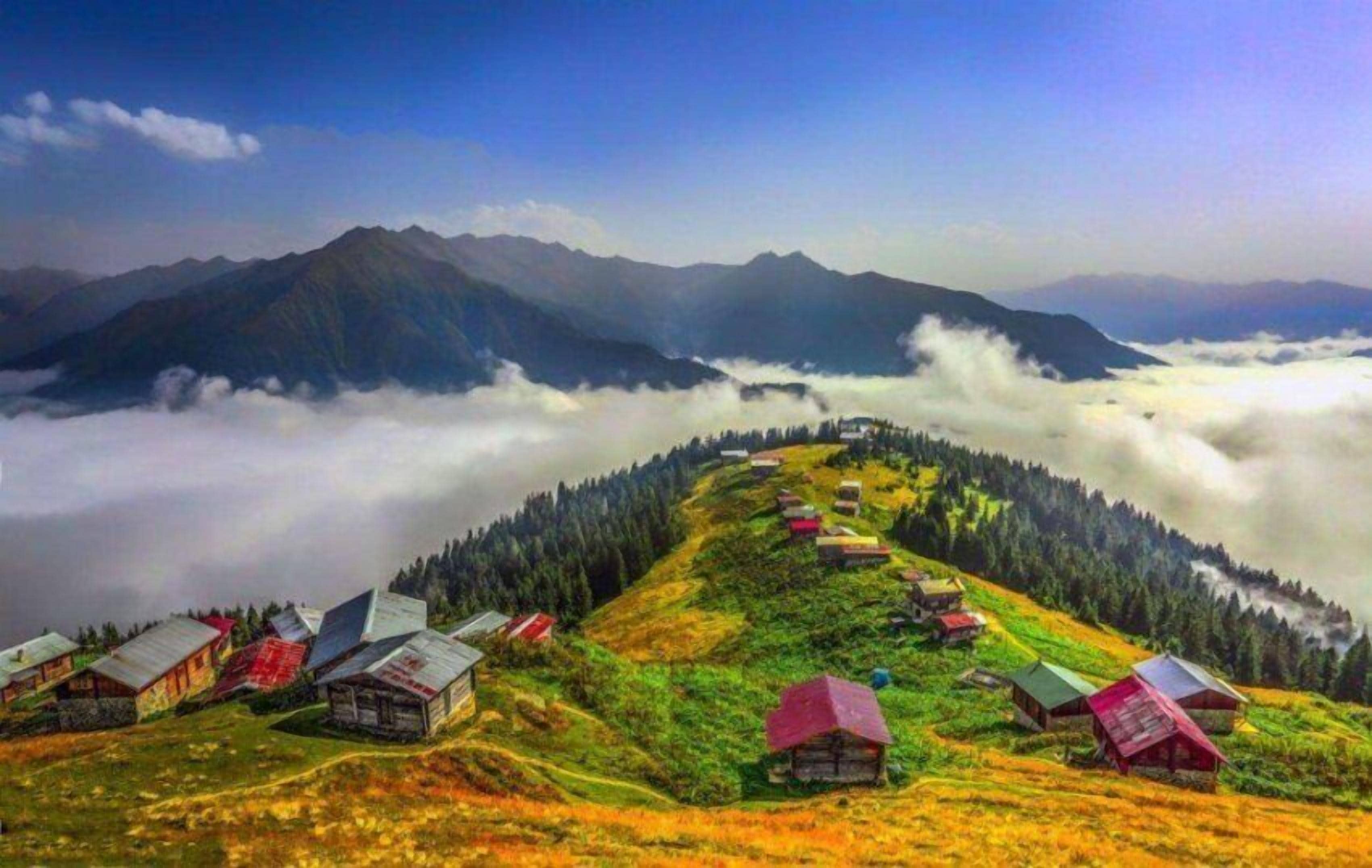 A mountain village with traditional houses, a clear sky, and a valley below shrouded in clouds.