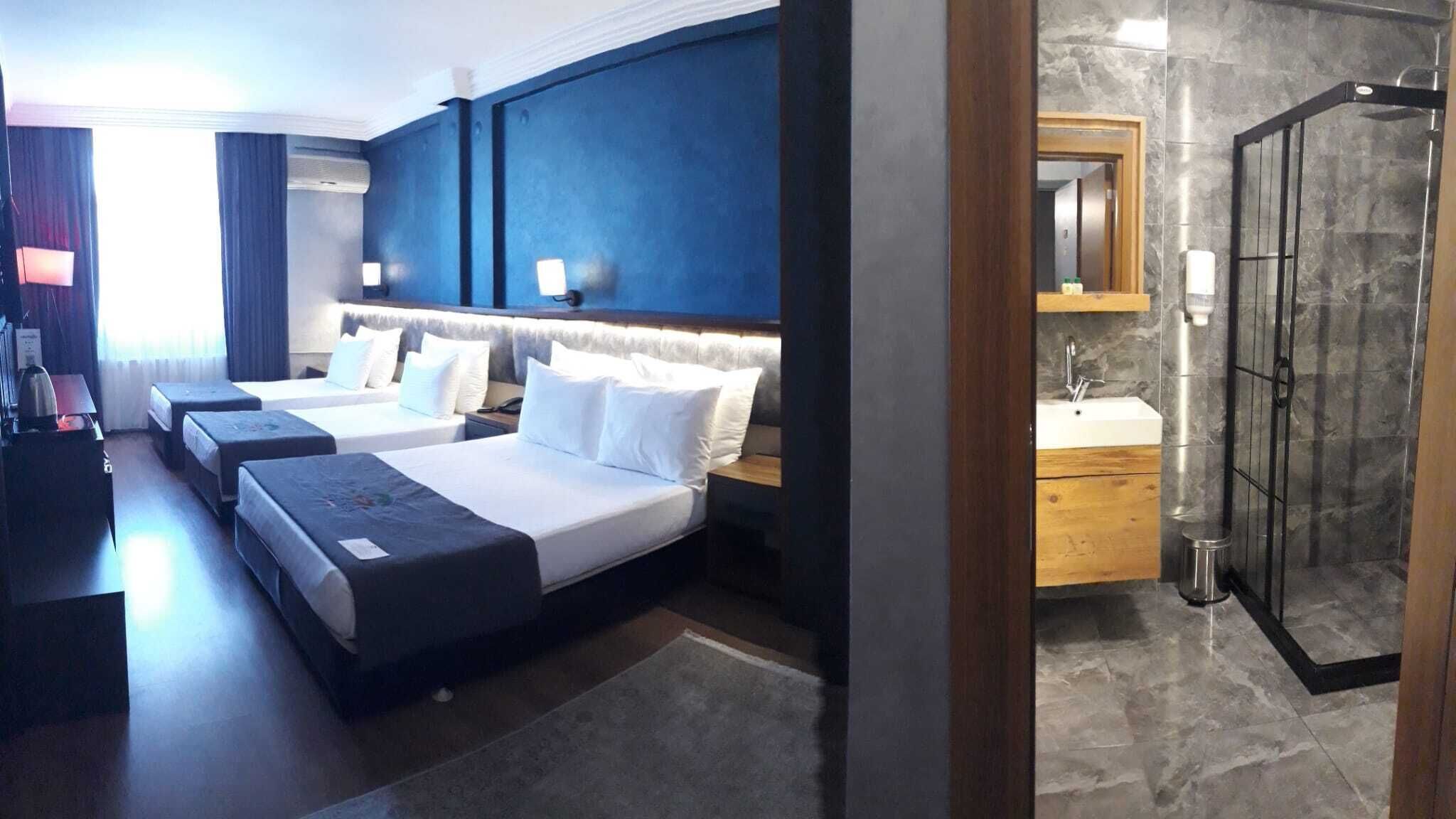 Une chambre d’hôtel avec deux lits, une salle de bain avec douche et un bureau avec une lampe.