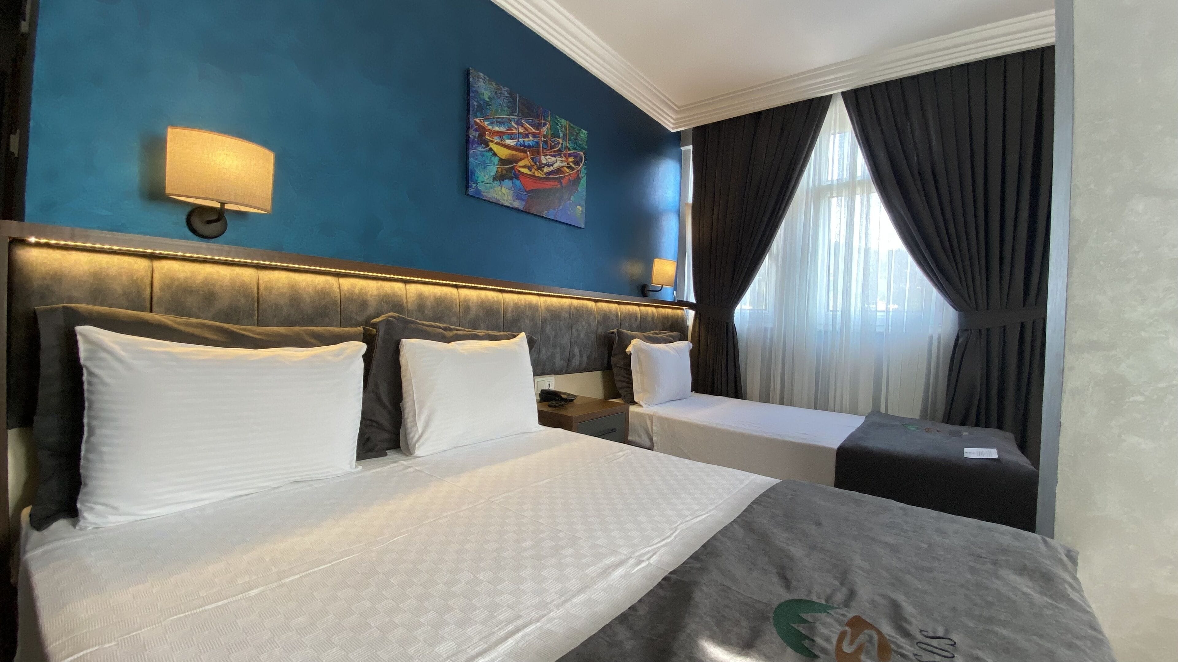 A hotel room with a large bed, two bedside tables, a painting on the wall, and a window with curtains.