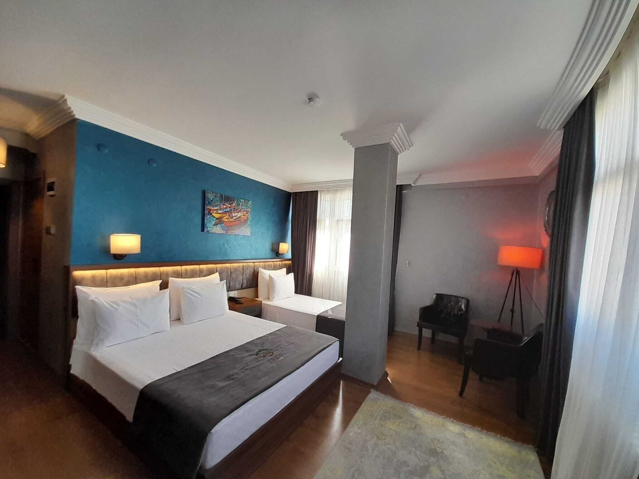 A hotel room with two beds, a desk, a chair, a lamp, and a painting on the wall.
