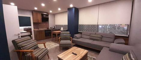Una sala de estar moderna con un sofá, sillones, una mesa de centro y una cocina al fondo.