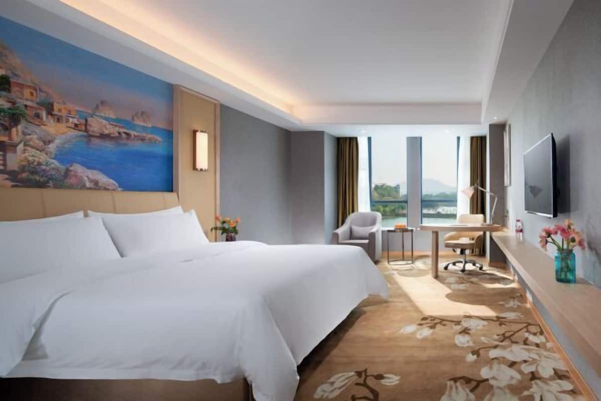 Una habitación de hotel con cama, escritorio, silla, televisor y un cuadro en la pared.