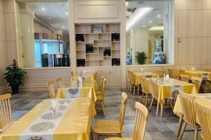 A restaurant with multiple tables and chairs, a decorative wall with shelves, and a large window.
