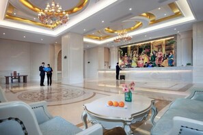 A hotel lobby with a reception desk, seating area, and a chandelier.