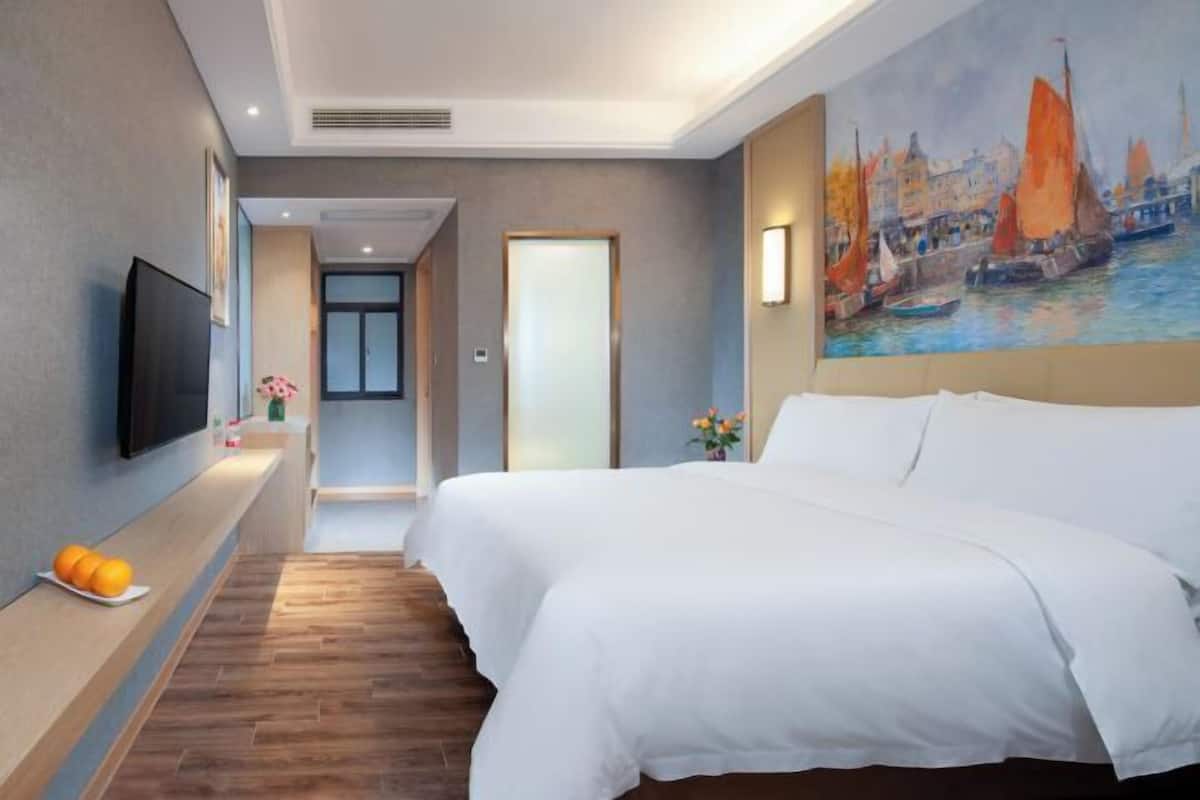 Habitación de hotel con una cama grande, un televisor de pantalla plana, un cuadro de una escena portuaria y piso de madera.