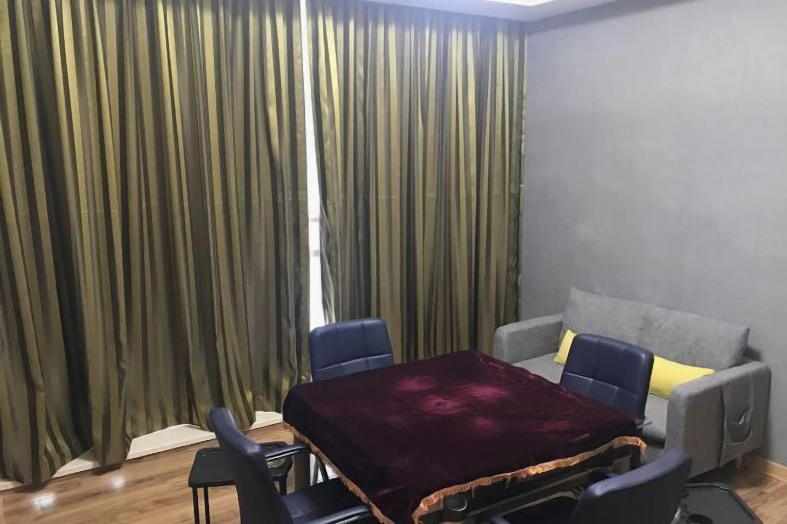 A room with a table covered by a dark cloth, two chairs, a sofa with cushions, and a curtain with vertical stripes.
