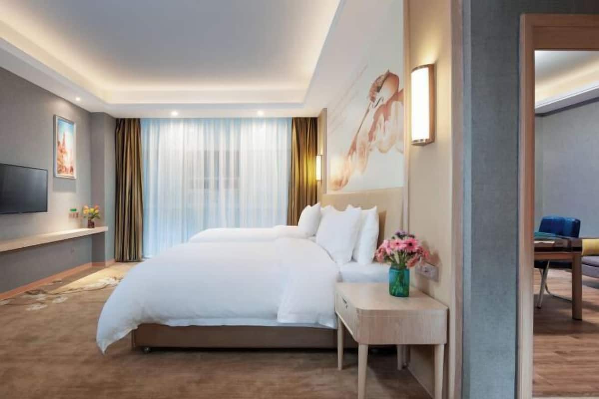 Habitación de hotel con una cama grande, una mesita de noche con un florero, un televisor de pantalla plana en la pared y vistas de la ciudad a través de la ventana.