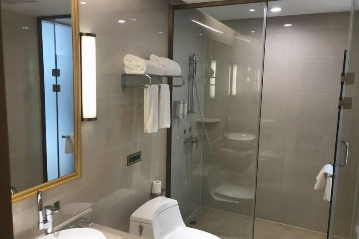 A modern bathroom with a glass-enclosed shower, a toilet, a sink, and a mirror with a gold frame.