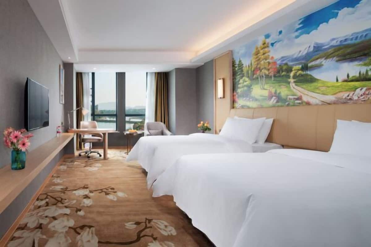 Una habitación de hotel con dos camas, un escritorio, una silla, un televisor y un ventanal grande.