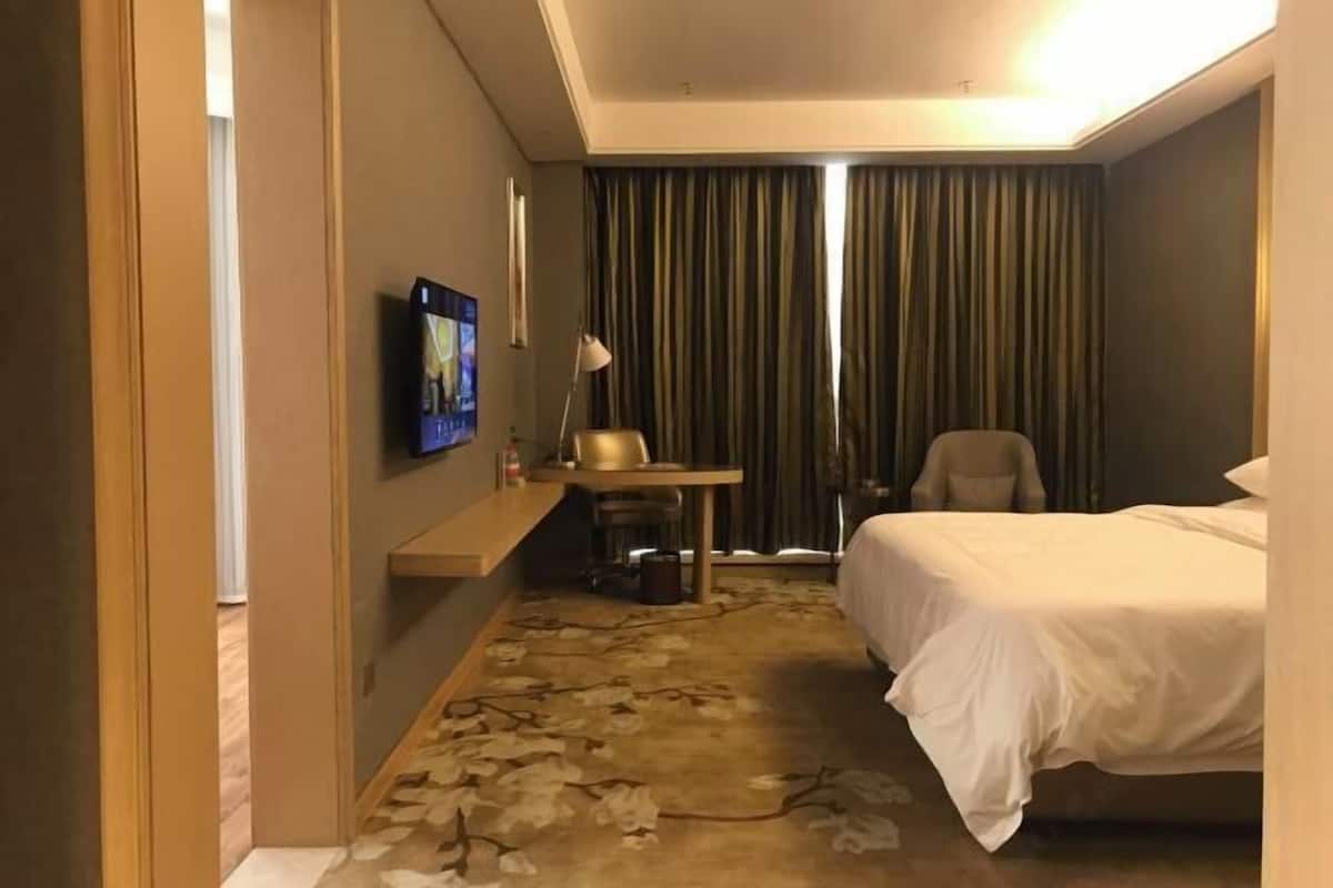 Habitación de hotel con cama, escritorio, silla, televisor y ventana con cortinas.