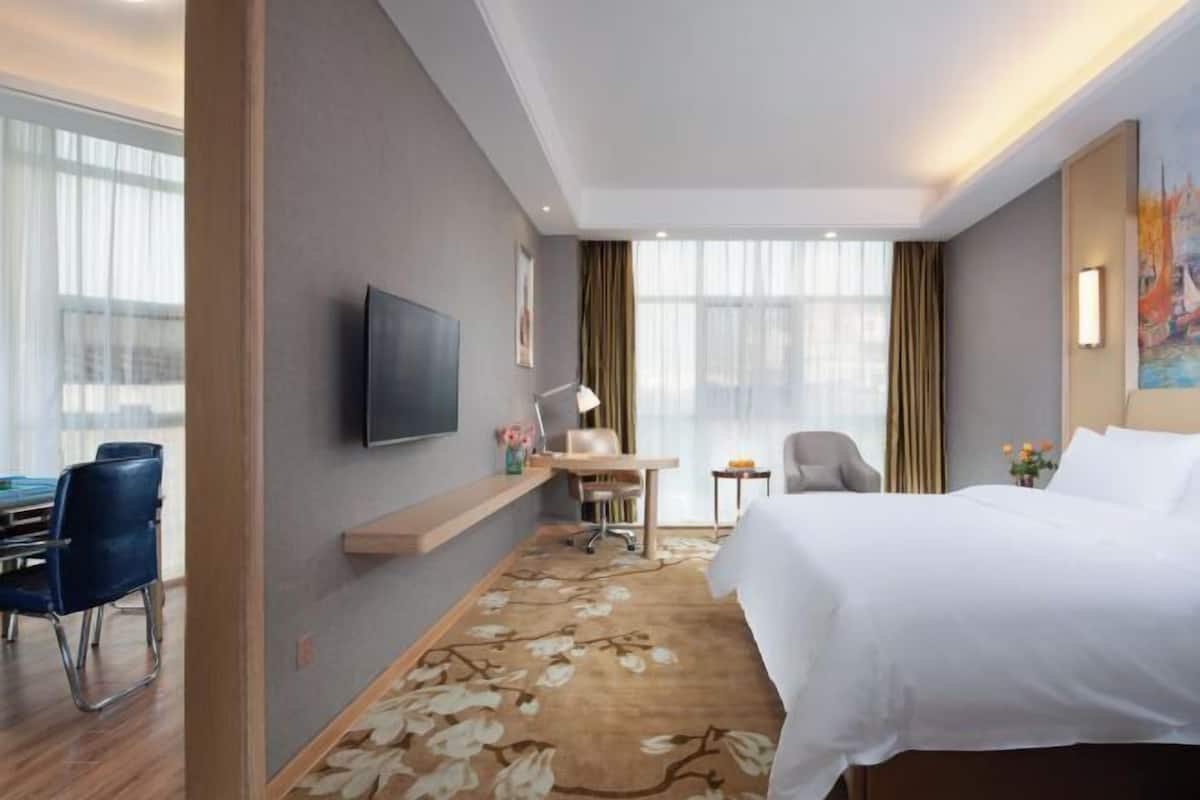 Habitación de hotel con cama, escritorio, silla, televisor y ventanas amplias.