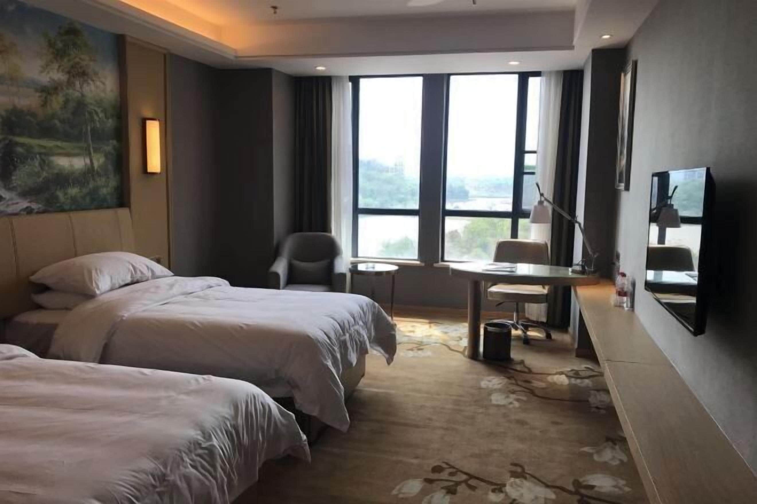 Ein Hotelzimmer mit zwei Betten, einem Schreibtisch, einem Sessel, einem Fernseher und einem großen Fenster mit Aussicht.