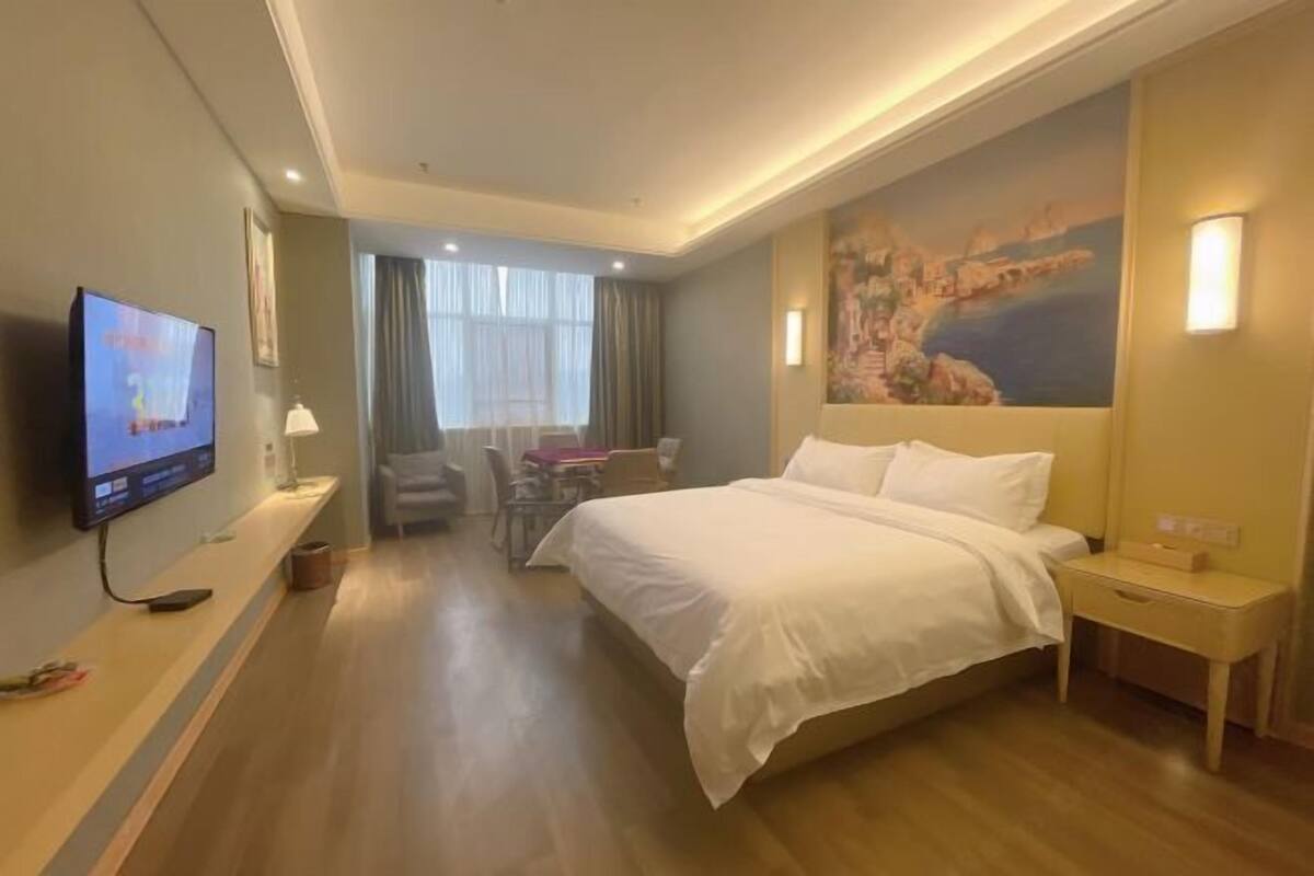 Habitación de hotel con una cama grande, un televisor en la pared, un escritorio con una silla y un cuadro en la pared.